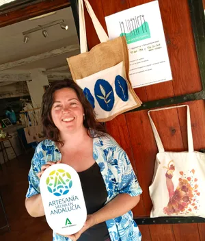 Clara Lanau delante de la tienda, con la placa de Artesanía hecha en Andalucía y sus bolsas de cianotipia