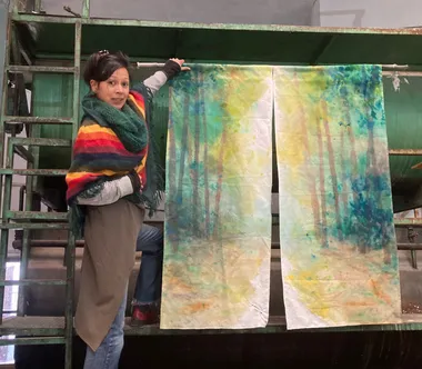 Marion Mieze en el taller, mostrando dos grandes telas pintadas con un bosque atravesado por la luz