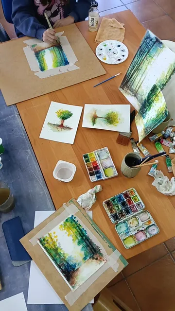 Mesa del taller de acuarela llena de paletas, pinceles y bosques pintados en acuarela