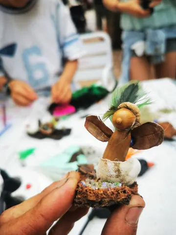 Un duende bellotín recién hecho, con bellota, vainas y plumas, sostenido en la mano durante el taller