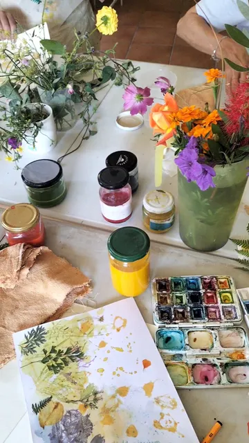 Mesa de pintura botánica con flores frescas, tarros de pigmentos y estampaciones de plantas