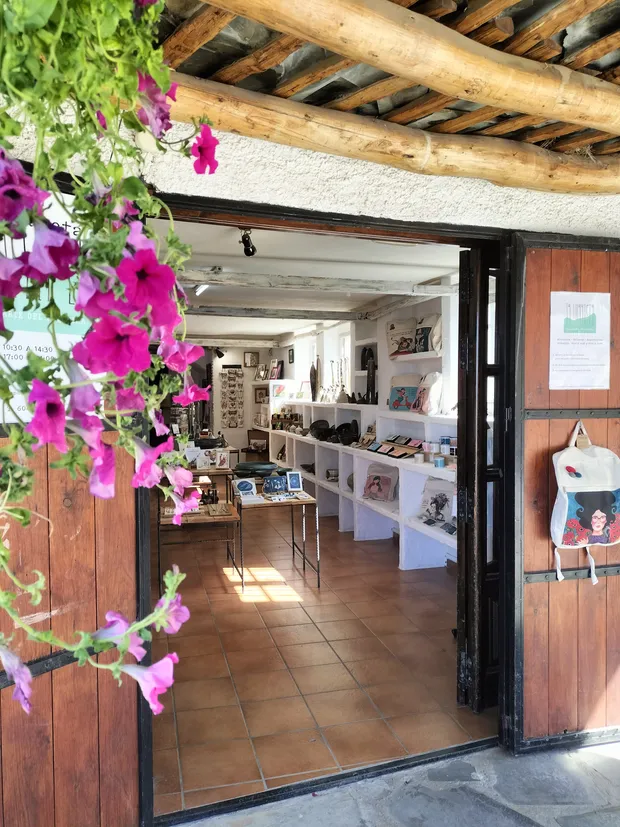 Las puertas abiertas de la tienda, con las estanterías de artesanía al fondo y petunias en la entrada